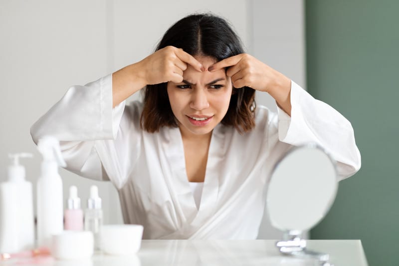 Young woman checking a red pimple on her face in the mirror before deciding how to treat it
