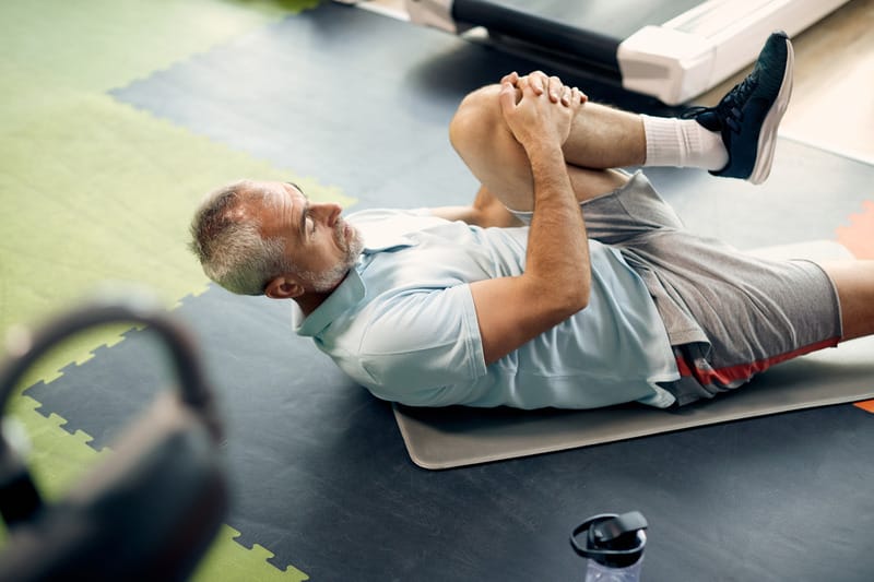 Man lying on his back doing a knee to chest stretch to gently release the lower back