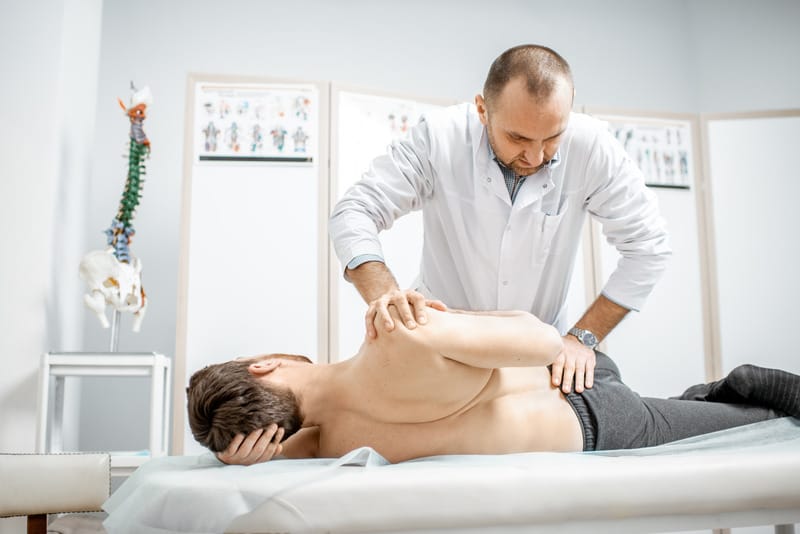 Physiotherapist assessing a patient's stiff back with hands-on treatment