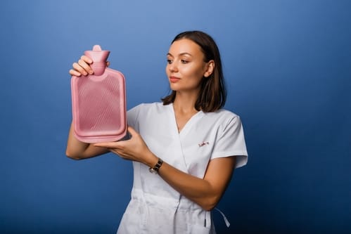 Woman in a medical gown holding a heating pad before a gynaecology procedure