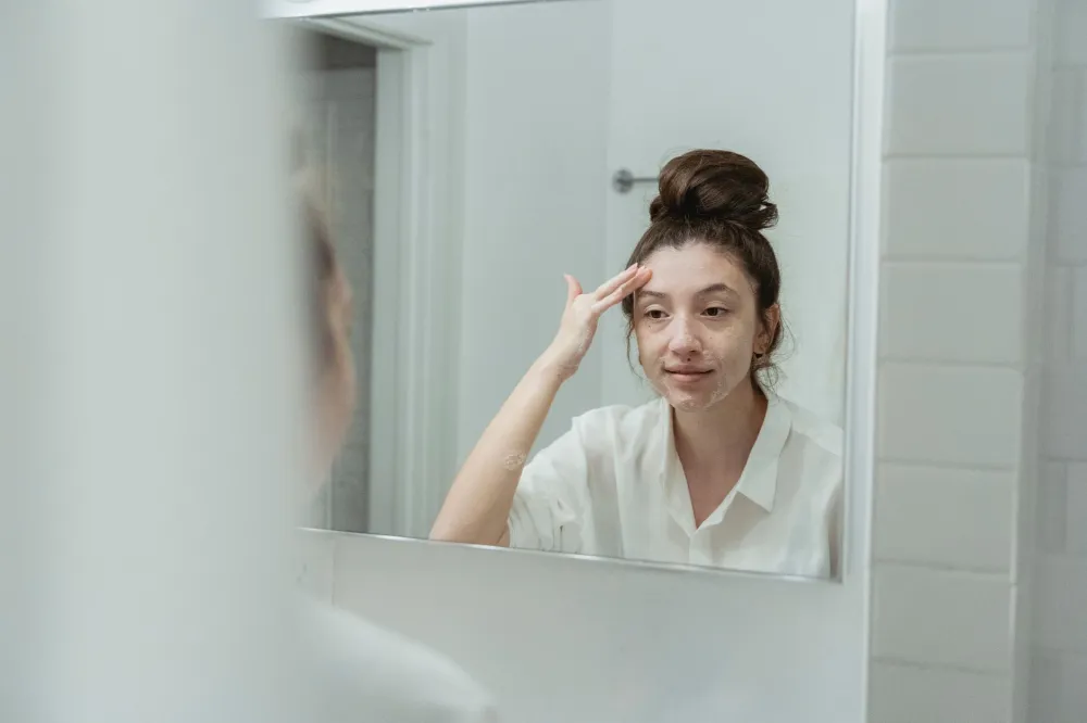 Woman applying retinol serum in bathroom mirror as part of an anti-aging skincare routine