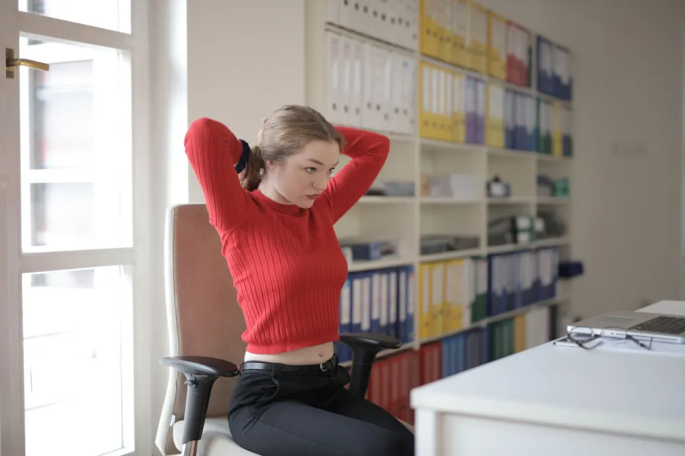 Desk Posture and Back Pain From Sitting All Day: What Works 4 Office worker doing seated back stretch at desk to relieve lower back pain from sitting