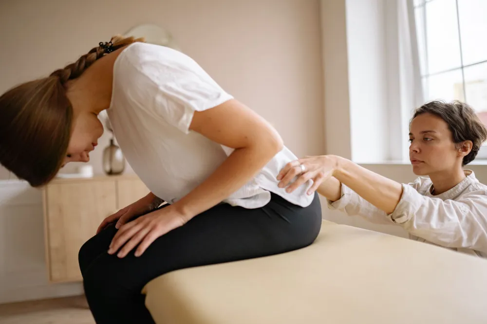 Desk Posture and Back Pain From Sitting All Day: What Works 5 Physical therapist assessing patient lower back pain caused by prolonged desk sitting