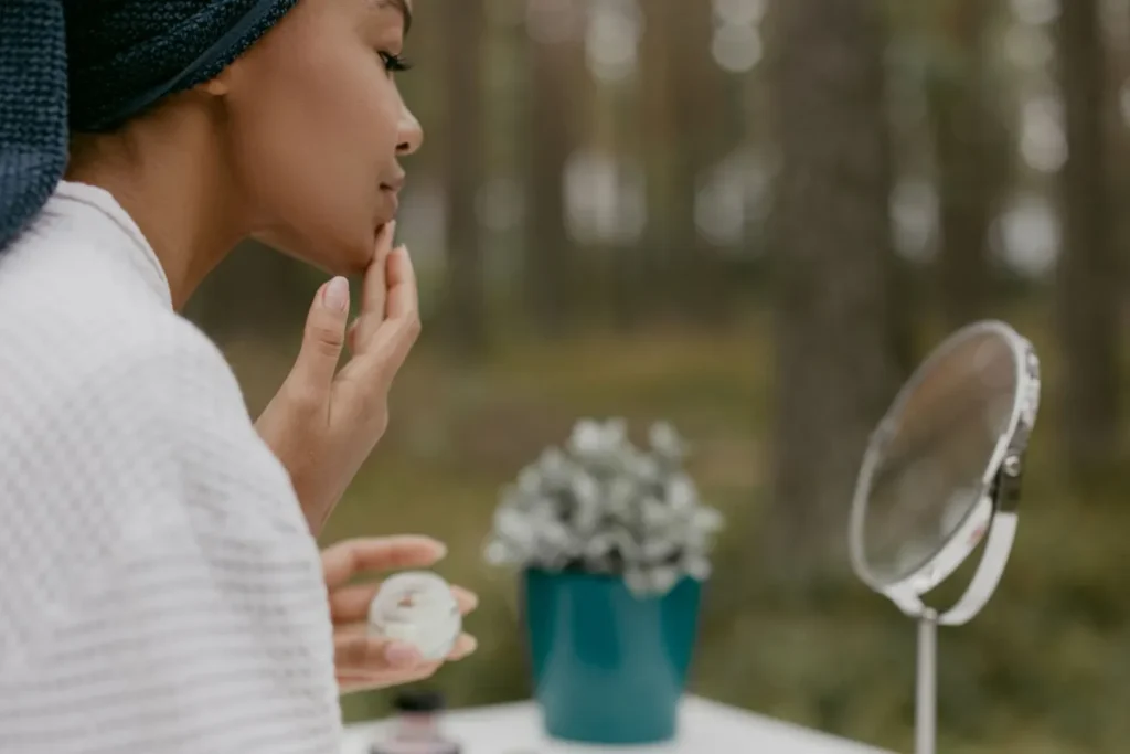 Dry Winter Skin: Fix Your Routine Before It Gets Worse 41 Woman applying thick moisturizer to dry winter skin in bathroom mirror