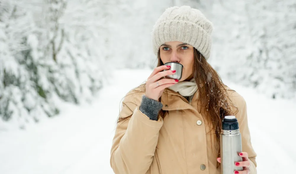 Woman holding warm mug near a cold window keeping skin hydrated in winter