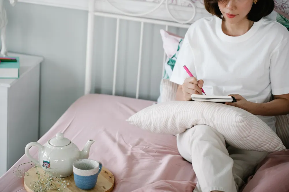 Woman writing in a journal at home as part of a chronic pain mental wellness routine