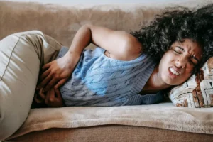 Young woman sitting on couch holding abdomen reflecting endometriosis mental health struggle