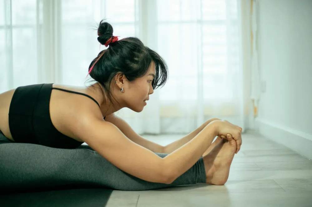 Woman in her 40s doing a hip-opening stretch on a yoga mat at home