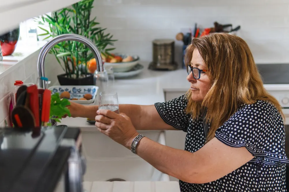 Person filling a reusable water bottle at a kitchen sink for daily hydration