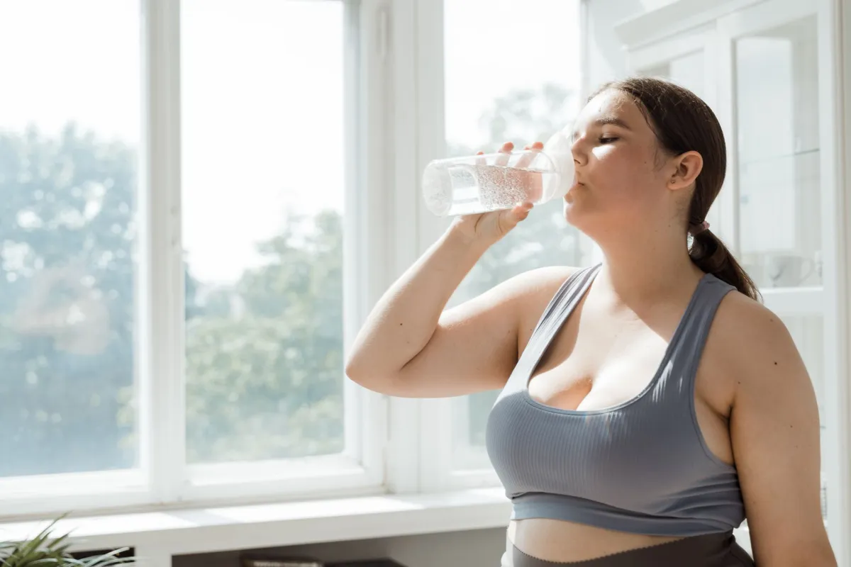Woman drinking a glass of water in natural sunlight, illustrating daily hydration needs
