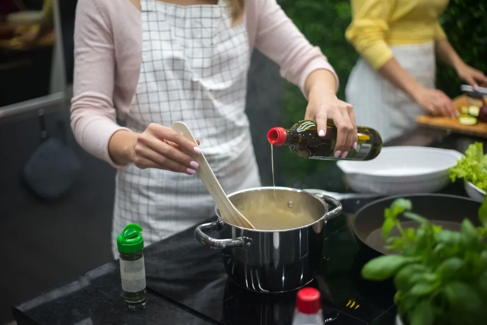 Person drizzling extra-virgin olive oil over fresh colorful vegetables for a Mediterranean meal
