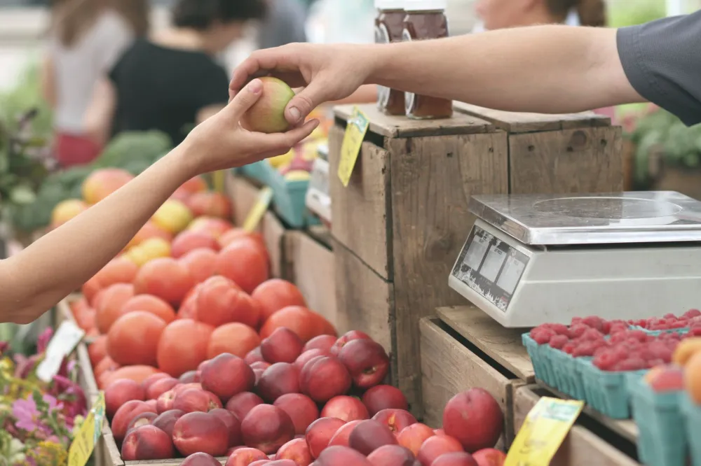 Woman choosing fresh seasonal produce at a farmers market for healthy Mediterranean eating