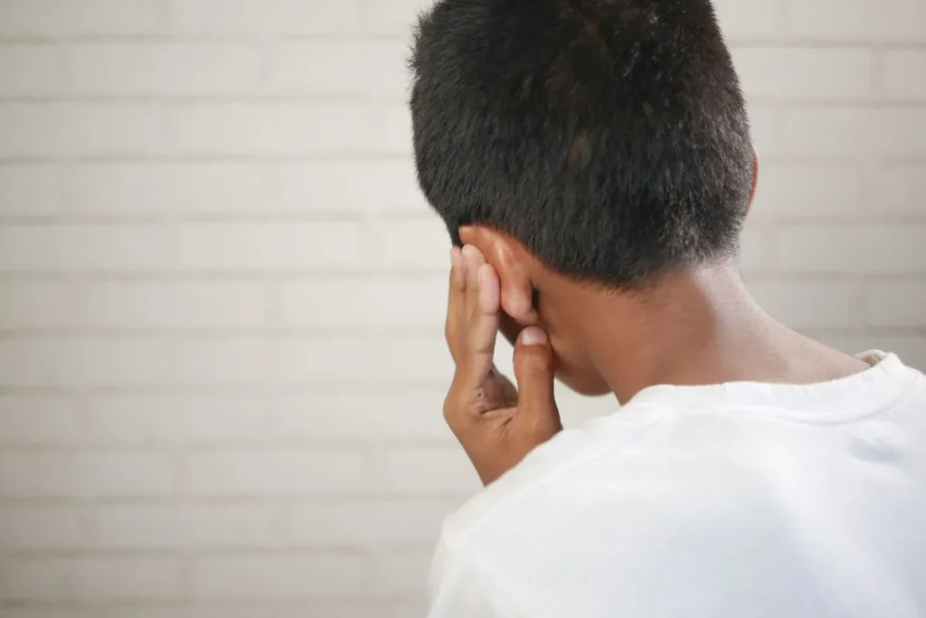 Adult pressing hand to ear experiencing tinnitus ringing sensation indoors