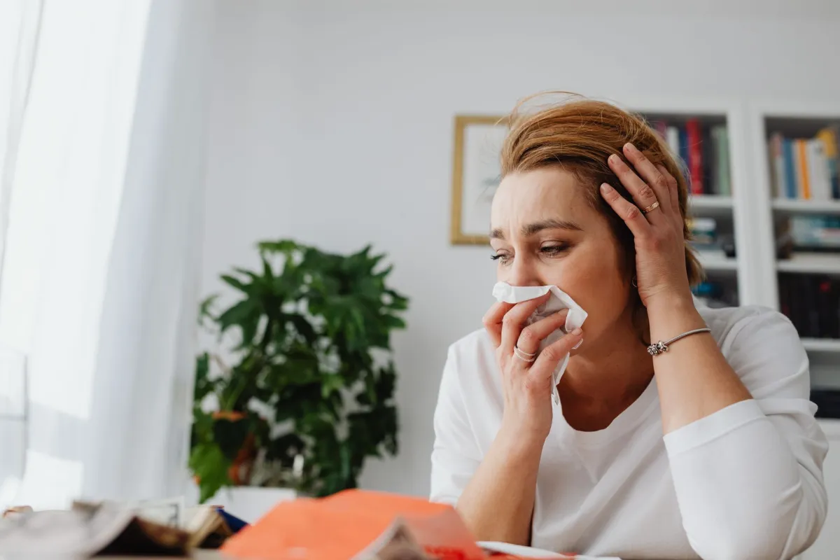 Person wrapped in blanket blowing nose, comparing flu cold and COVID symptoms