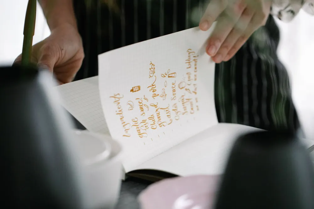 Person writing a simple weekly meal plan in a notepad beside fresh produce