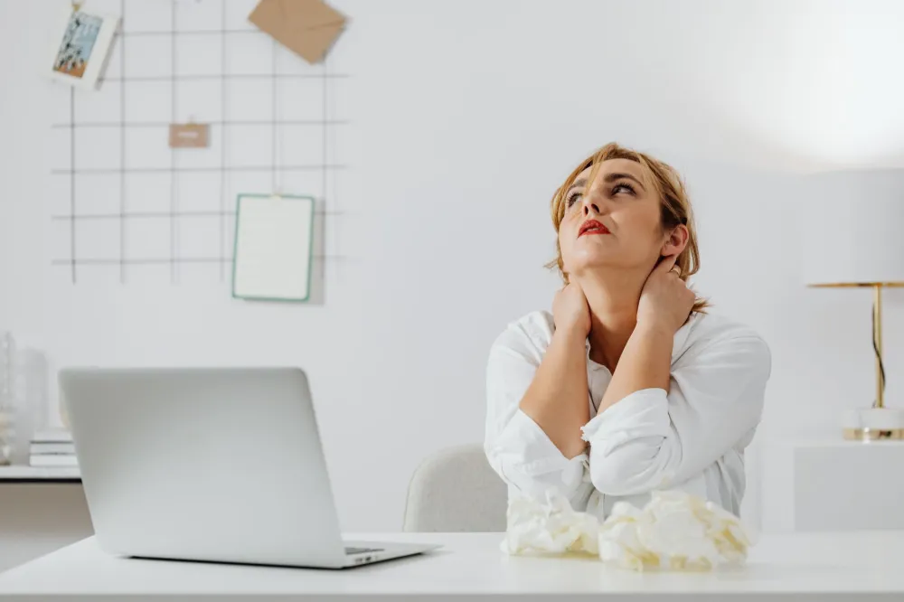 Office worker stretching stiff neck at desk, a common source of daytime neck pain