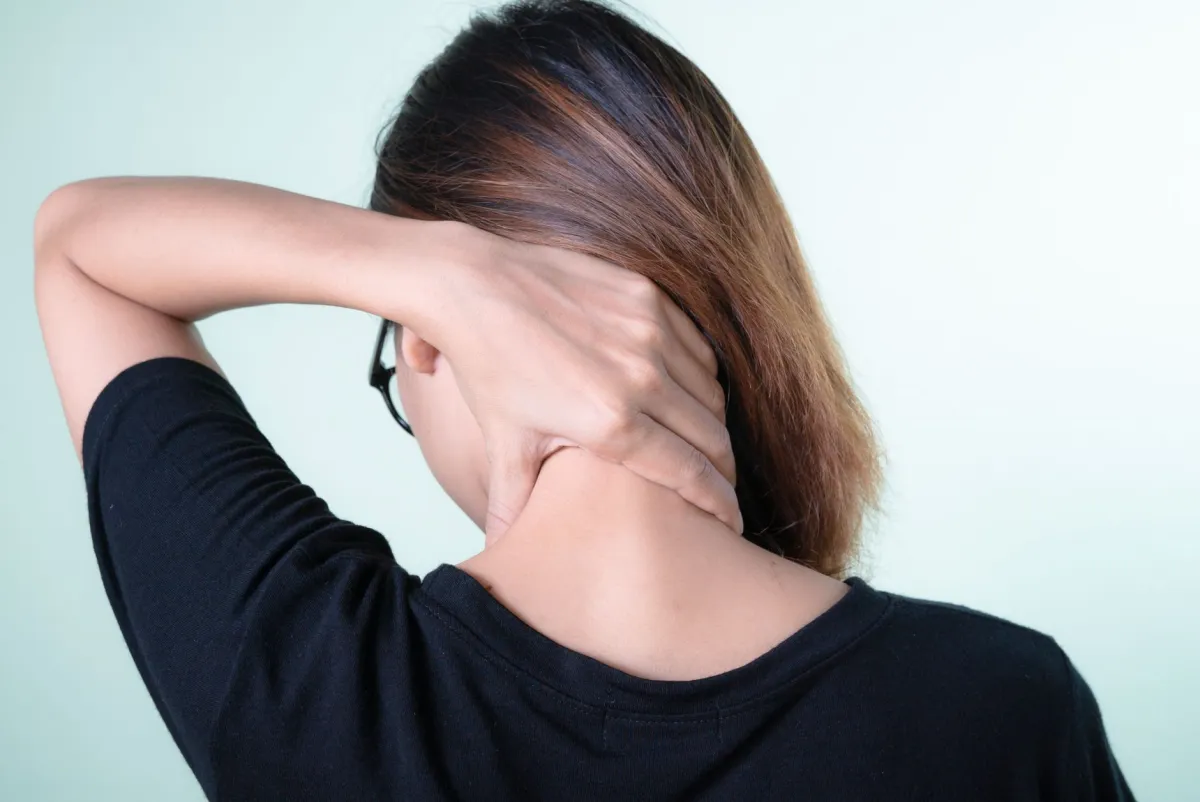 Woman holding her neck in pain after waking up, needing a better pillow for neck pain