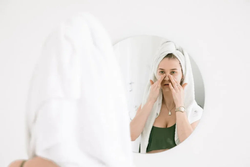 Woman applying retinol serum to face in bathroom mirror as part of her skin care routine