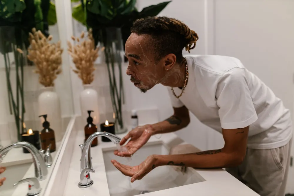 woman gently cleansing her face over a sink as first skincare routine step
