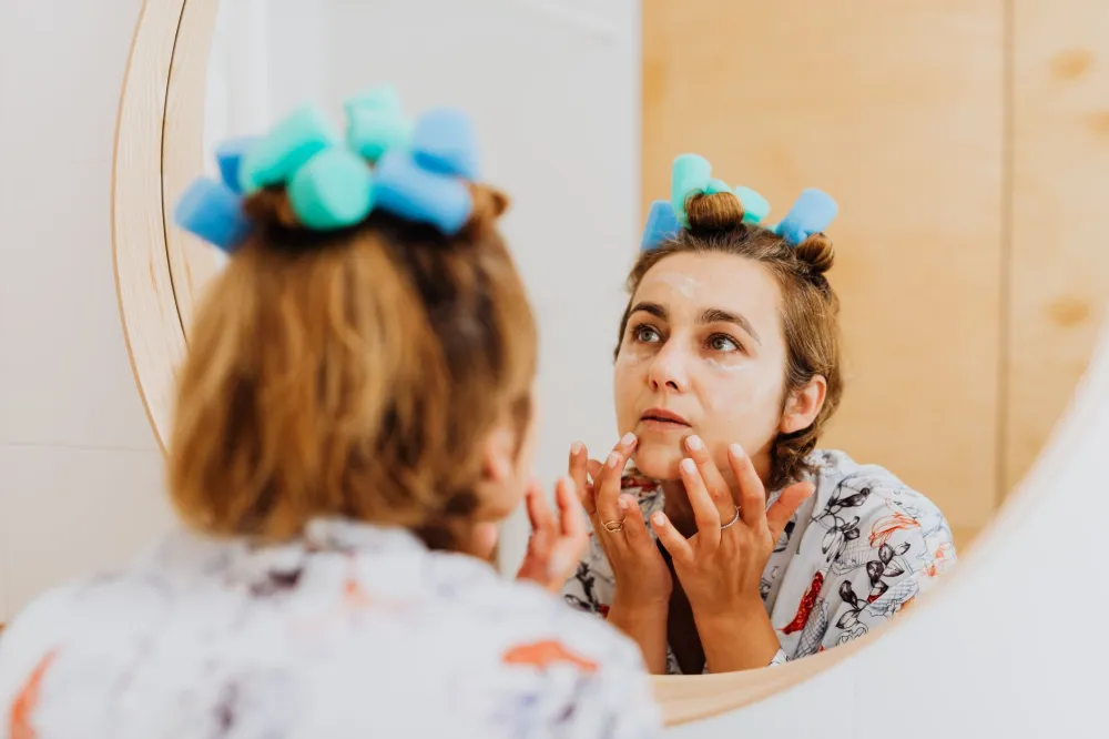 woman applying retinol night cream in mirror as part of correct evening skincare order