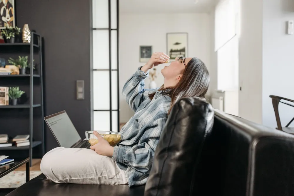 Stressed person reaching for junk food at a desk, stress-driven overeating habit