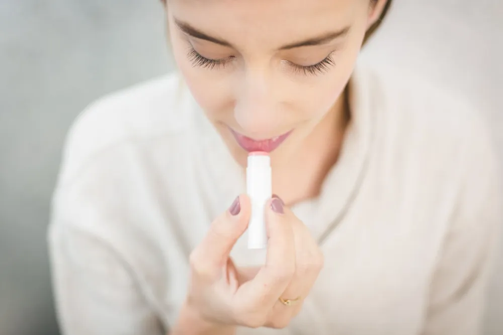 Person gently applying lip balm to moisturize lips and avoid irritating skin bumps