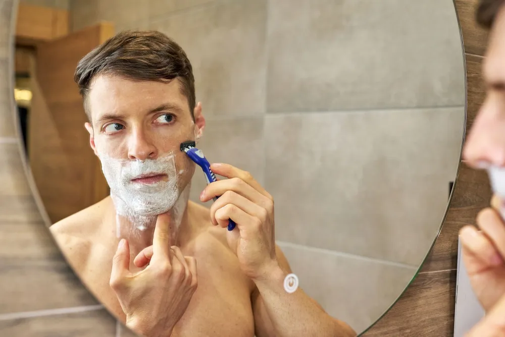 Man shaving in a bright bathroom, a common trigger for genital pimples