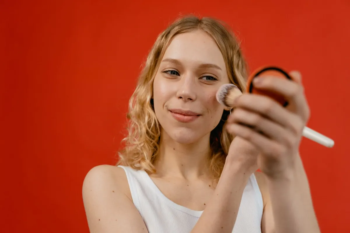 Young woman applying concealer to her neck to hide a hickey