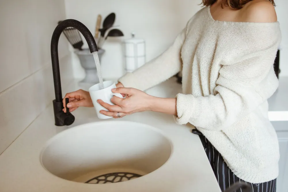 Woman drinking a glass of water in a bright kitchen during early ketosis