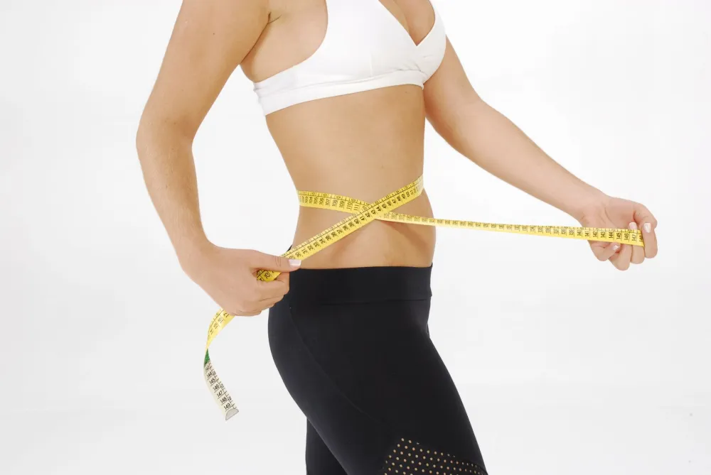 Woman measuring her waist at home to track keto results after four weeks