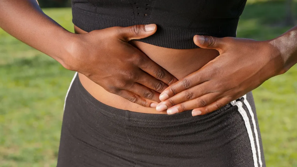 Woman sitting on a couch with her hand on her belly, feeling lower abdominal pain
